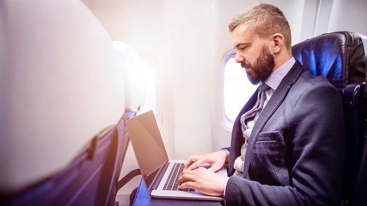 Mann arbeitet am HubSpot CRM im Flugzeug auf seinem Laptop